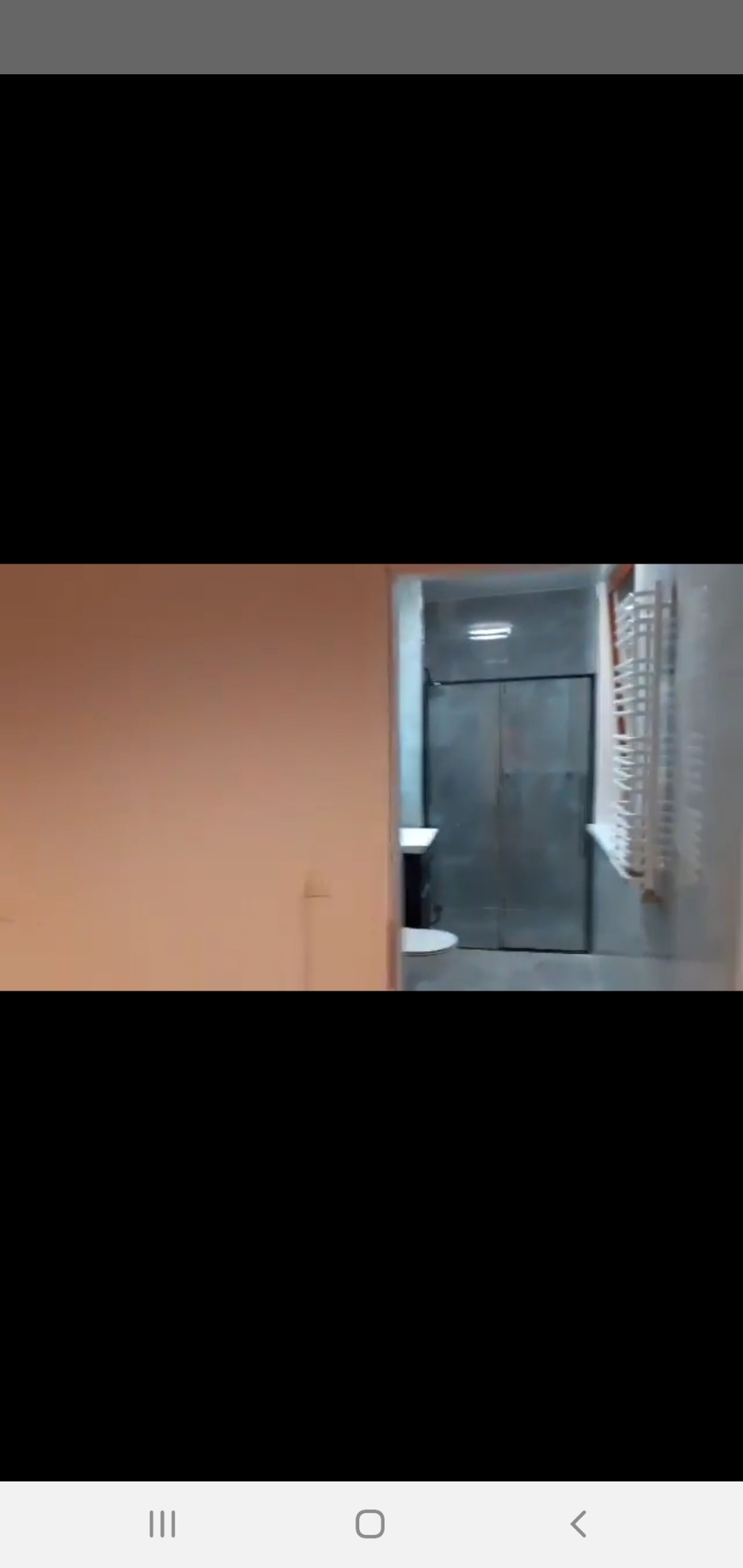 Widok na wyremontowaną łazienkę z szarą kabiną prysznicową i grzejnikiem drabinkowym, widoczne fragmenty umywalki i pomarańczowej ściany.