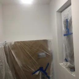 Świeżo pomalowane na biało wnętrze łazienki z zabezpieczonymi folią i taśmą malarską elementami przed zabrudzeniem.