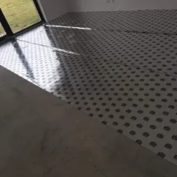 Przygotowanie podłoża pod płytki: rozłożona folia ochronna z nadrukiem na betonowej wylewce w nowym budynku, widok z okna.