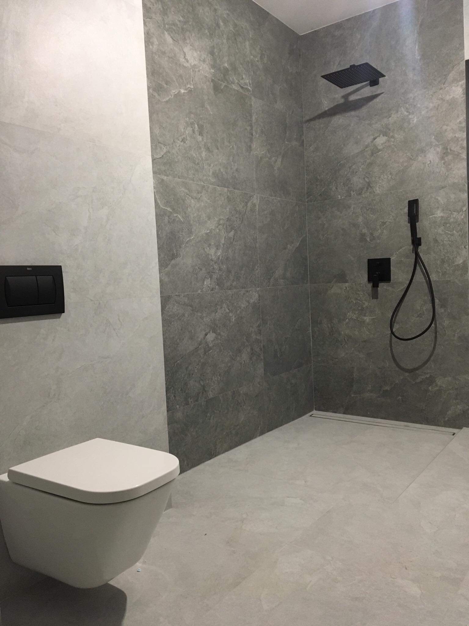 Nowoczesna łazienka w Żyrardowie z szarymi płytkami imitującymi kamień, czarną armaturą i podwieszaną toaletą.