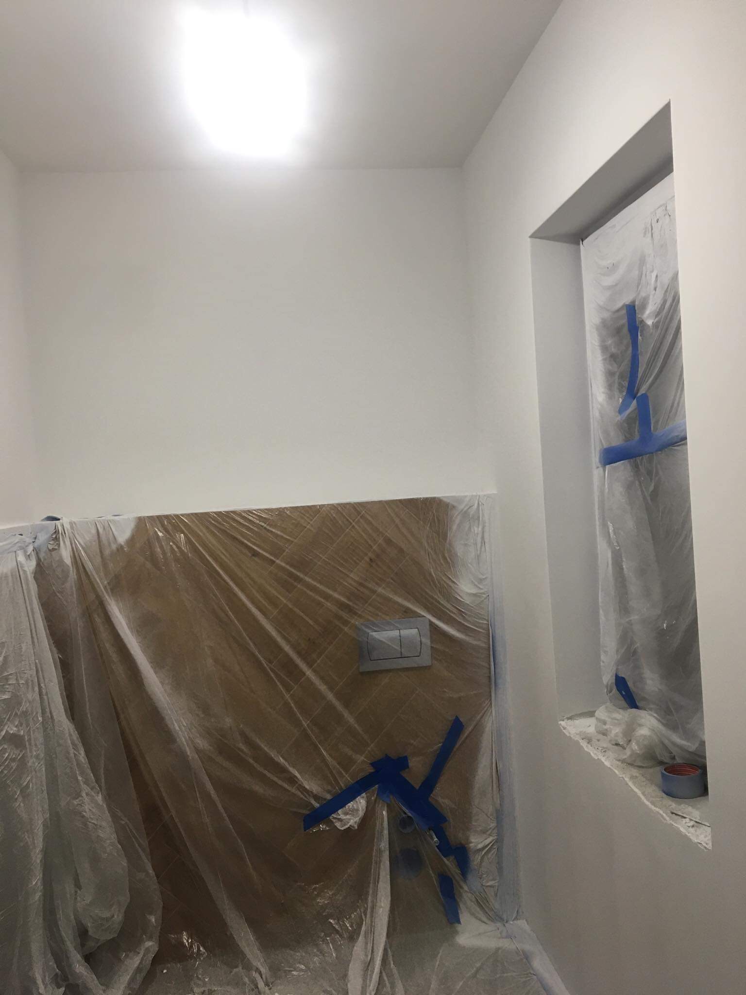 Świeżo pomalowane na biało wnętrze łazienki z zabezpieczonymi folią i taśmą malarską elementami przed zabrudzeniem.