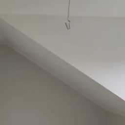 Świeżo pomalowane poddasze ze skosem, widoczne okno z ramą Drutex i haczyk na suficie, jasne, jednolite kolory.