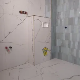 Surowy stan łazienki z marmurowymi płytkami ściennymi i podłogowymi w odcieniach bieli i szarości, z widocznymi przyłączami hydraulicznymi i elektrycznymi, oraz fragmentem ściany wykończonej...