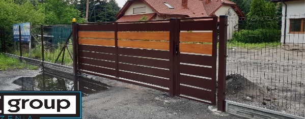 Nowoczesna brama przesuwna z brązowymi, poziomymi panelami metalowymi i wstawkami z jasnego drewna, widoczna z zewnątrz posesji, z fragmentem ogrodzenia panelowego w tle.