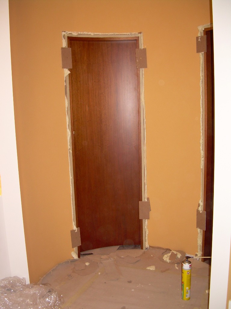 Montaż brązowych drzwi wewnętrznych z pianką montażową w futrynie, zabezpieczone kartonem, widoczna puszka pianki na podłodze.