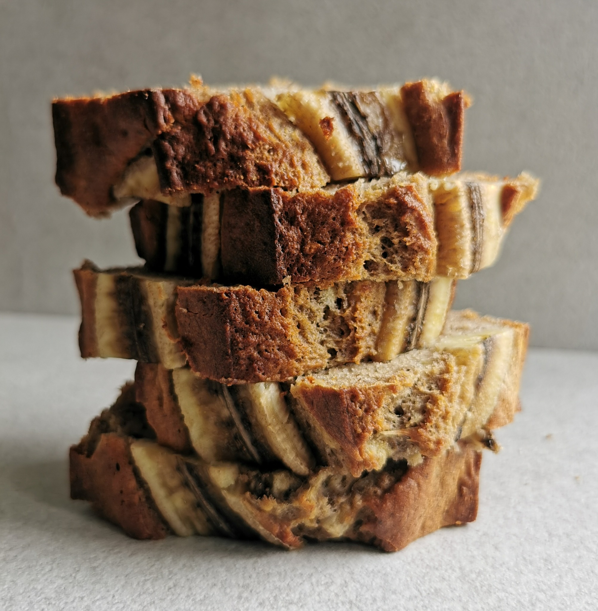 Stos ułożonych kromek domowego chleba bananowego z widoczną strukturą miąższu i skórki, na neutralnym tle.
