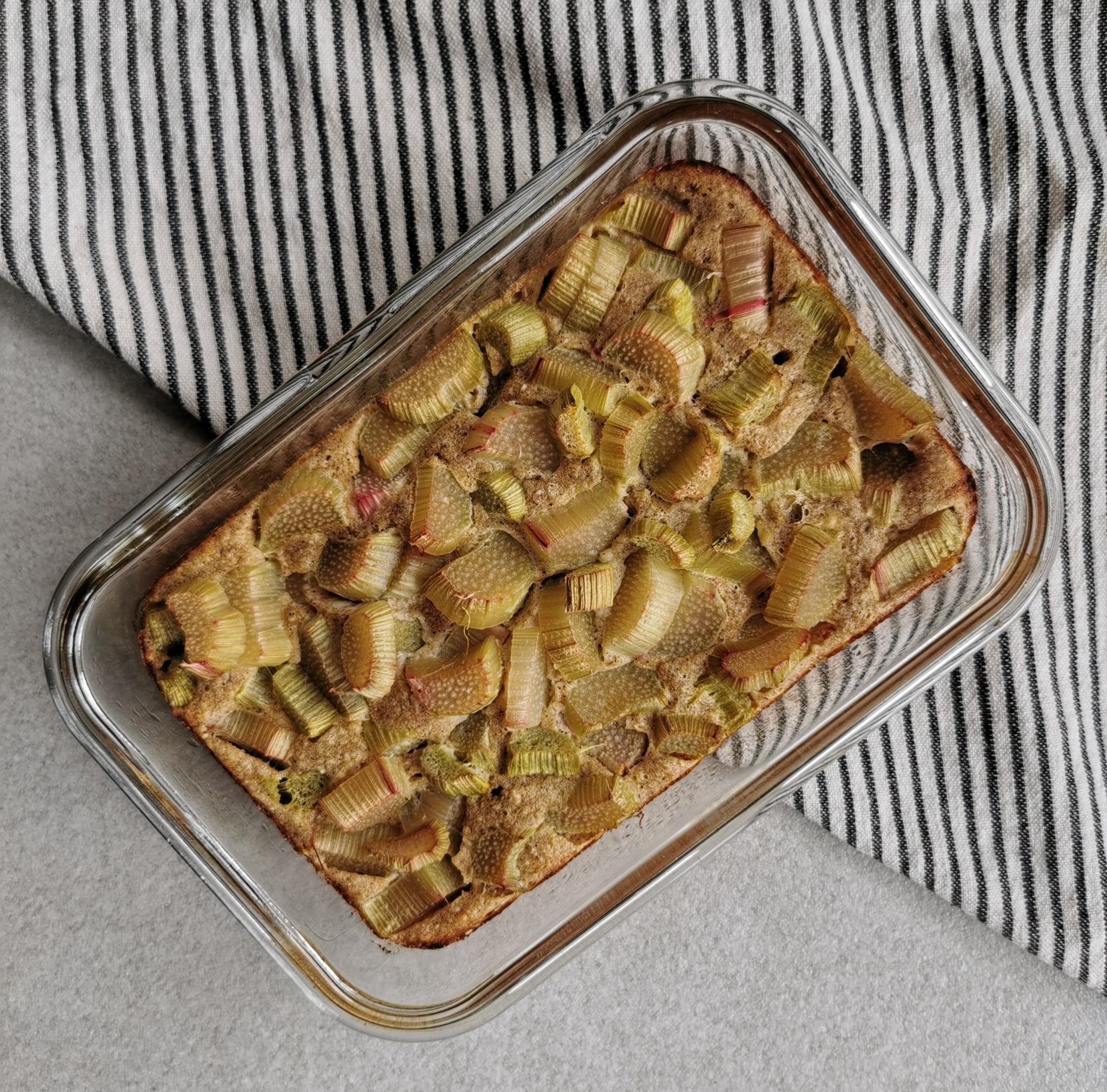 Keks z rabarbarem w szklanym naczyniu żaroodpornym, widok z góry, tło w czarno-białe paski.