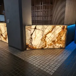 Podświetlany od wewnątrz panel z onyksu z wyraźnym żyłkowaniem, tworzący element dekoracyjny baru lub recepcji w nowoczesnym wnętrzu, z widoczną strukturą kamienia i podświetleniem LED.