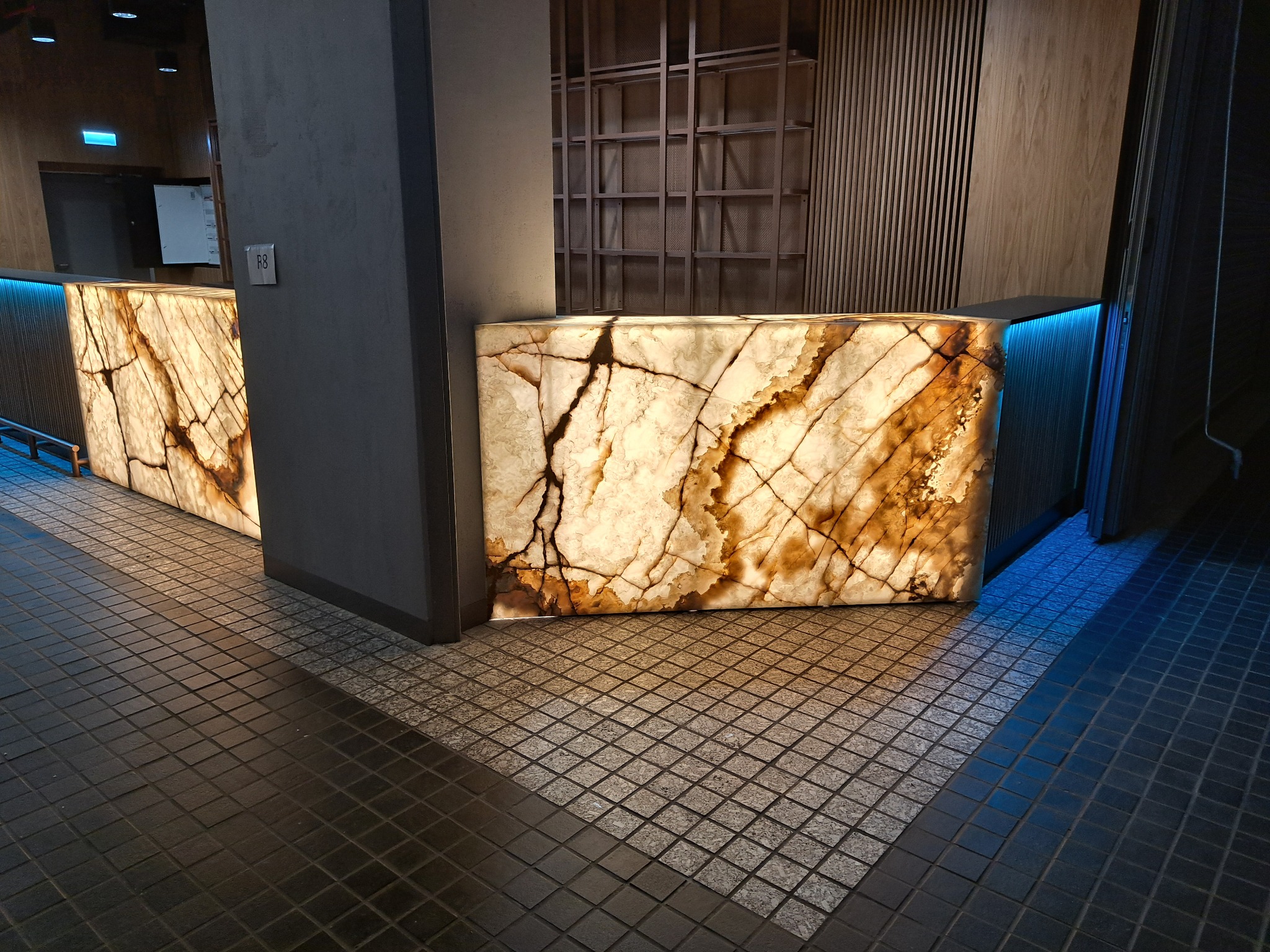 Podświetlany od wewnątrz panel z onyksu z wyraźnym żyłkowaniem, tworzący element dekoracyjny baru lub recepcji w nowoczesnym wnętrzu, z widoczną strukturą kamienia i podświetleniem LED.
