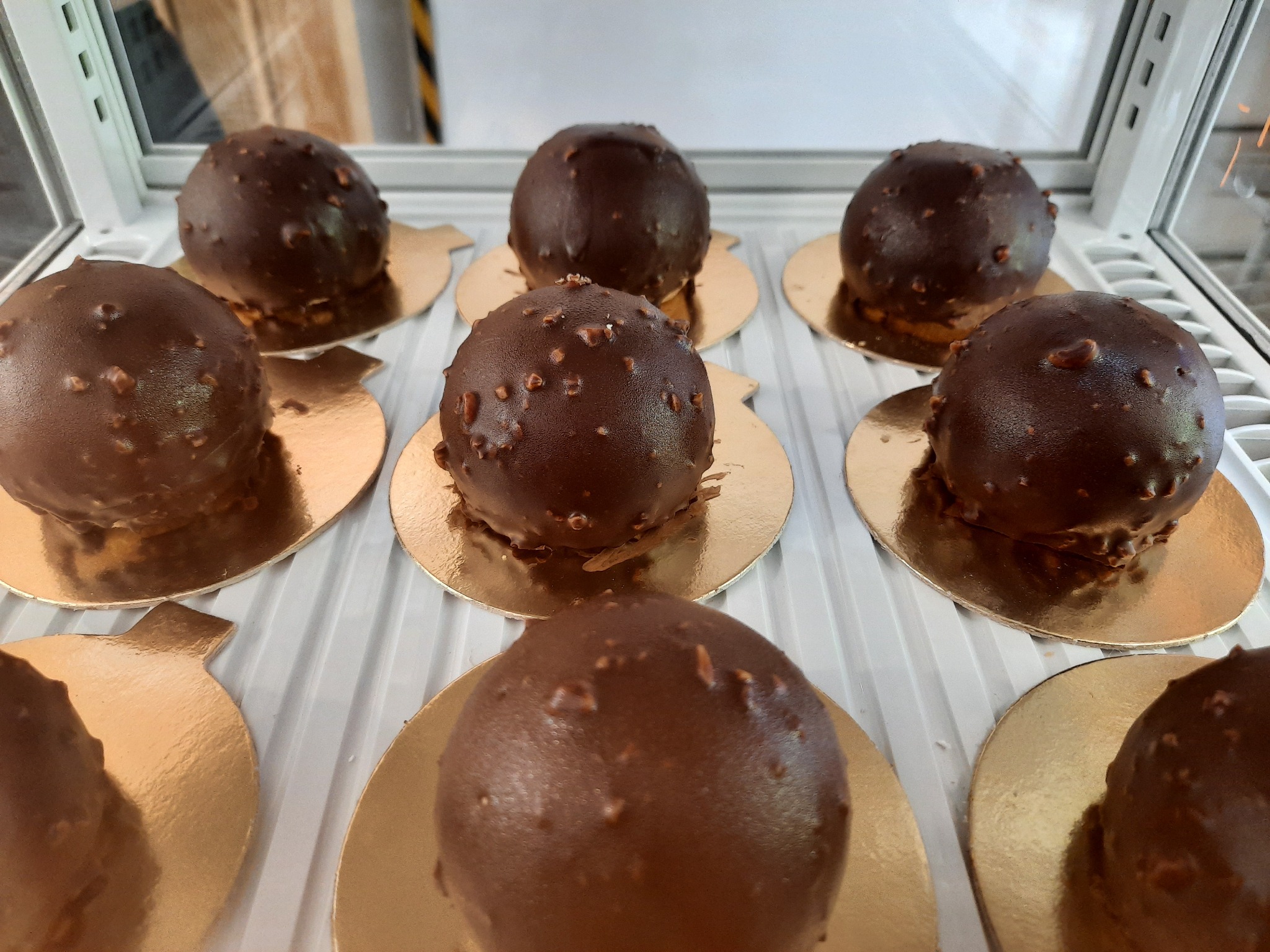 Rząd czekoladowych kulek z orzechami, umieszczonych na złotych podkładkach w chłodnej witrynie ekspozycyjnej.