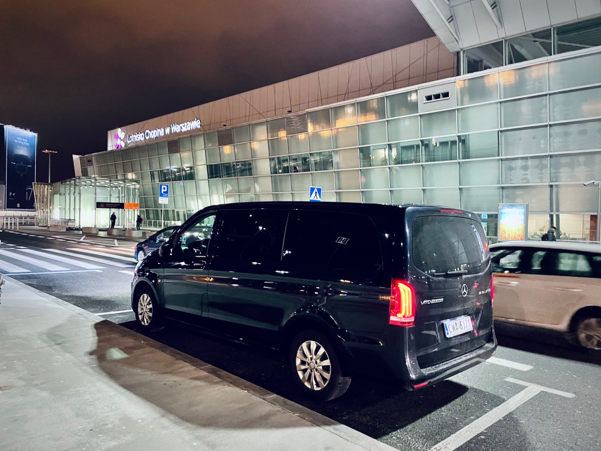 Czarny van Mercedes-Benz Vito Tourer zaparkowany przed Lotniskiem Chopina w Warszawie nocą, widoczny numer rejestracyjny CWA 6171.