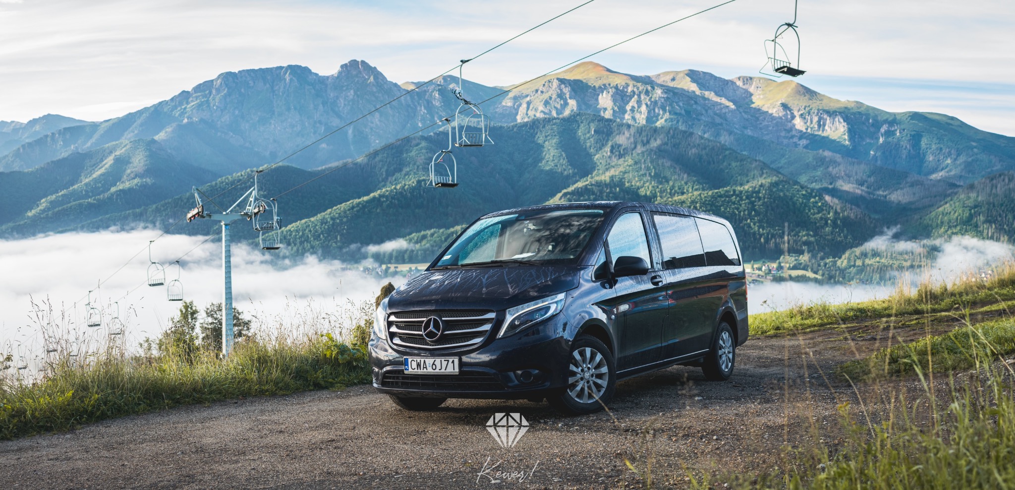 Czarny Mercedes V-klasy na tle górskiego krajobrazu z wyciągiem krzesełkowym, widok z lekkiej górki.