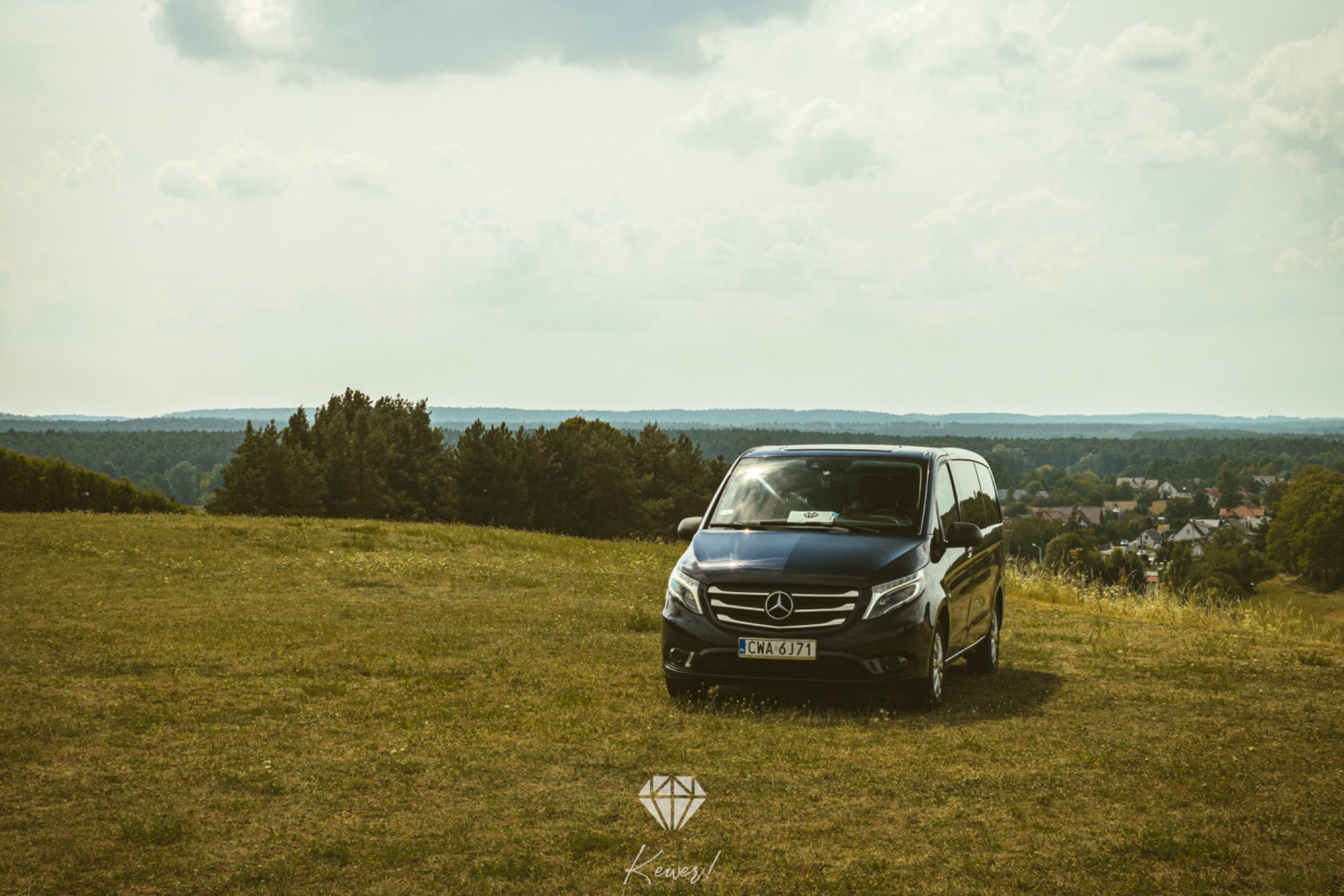 Czarny Mercedes Vito z polską tablicą rejestracyjną CWA 6J71, zaparkowany na wzgórzu z widokiem na las i zabudowania w oddali.