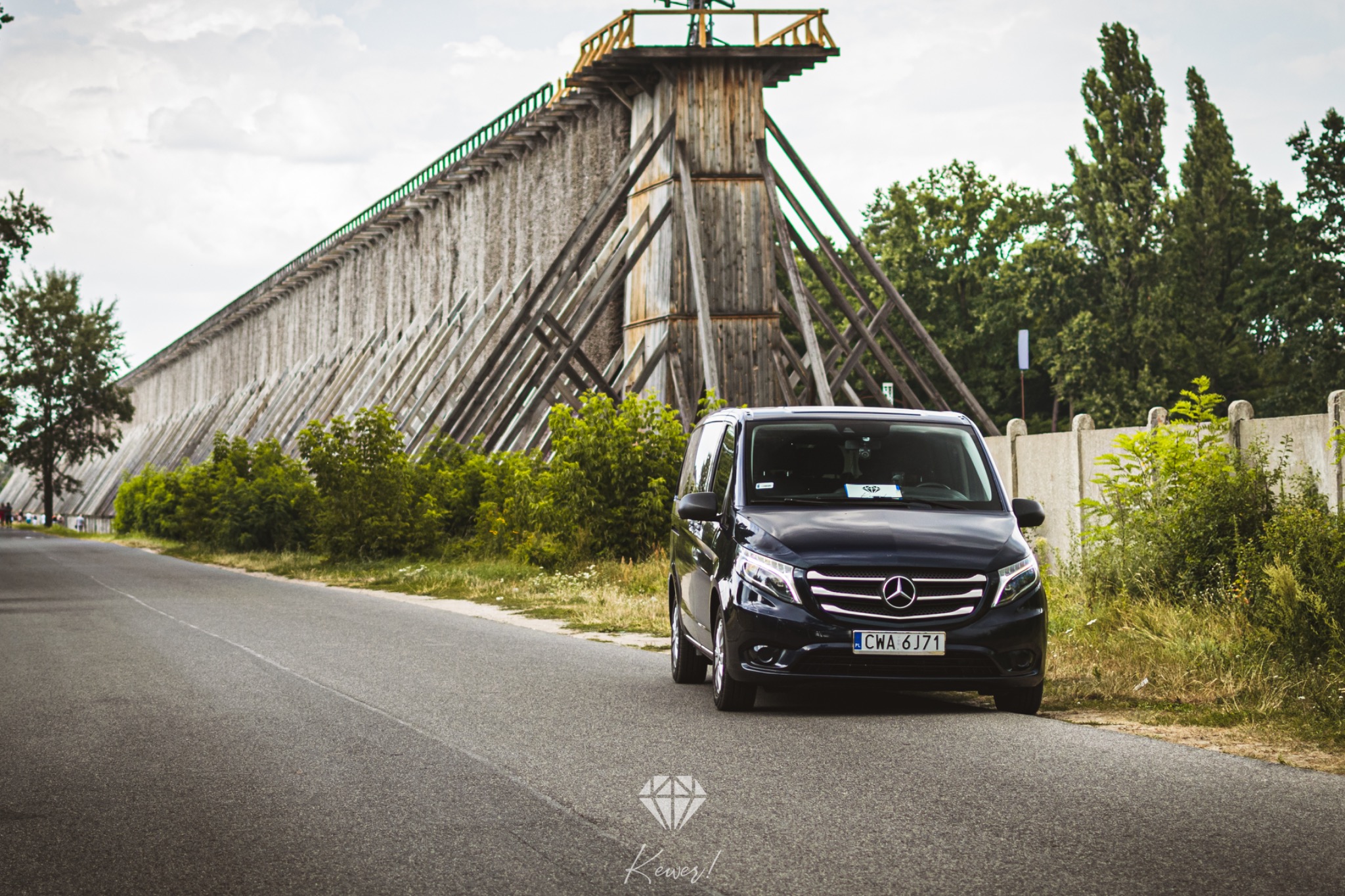 Czarny van Mercedes z polską tablicą rejestracyjną CWA 6J71 zaparkowany na drodze, w tle tężnie solankowe Ciechocinek.