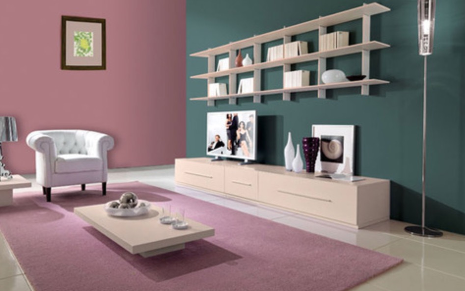 Nowoczesny salon z różowymi ścianami i wykładziną, zieloną ścianą z półkami, beżową szafką RTV i białym fotelem.