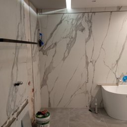 Rad-rud-system - Łazienka w trakcie remontu: płytki imitujące marmur na ścianach, biała wanna wolnostojąca, widoczny wiadro z zaprawą i narzędzia glazurnicze.