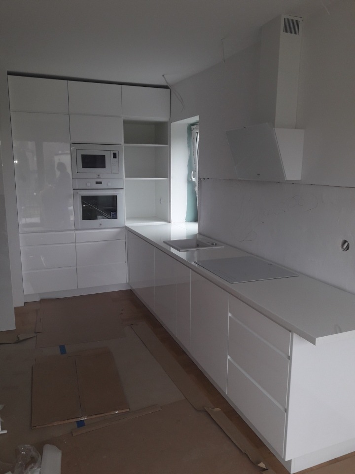 Nowoczesna, biała kuchnia z błyszczącymi frontami szafek i zabudowanym sprzętem AGD, na podłodze kartony zabezpieczające podczas prac.