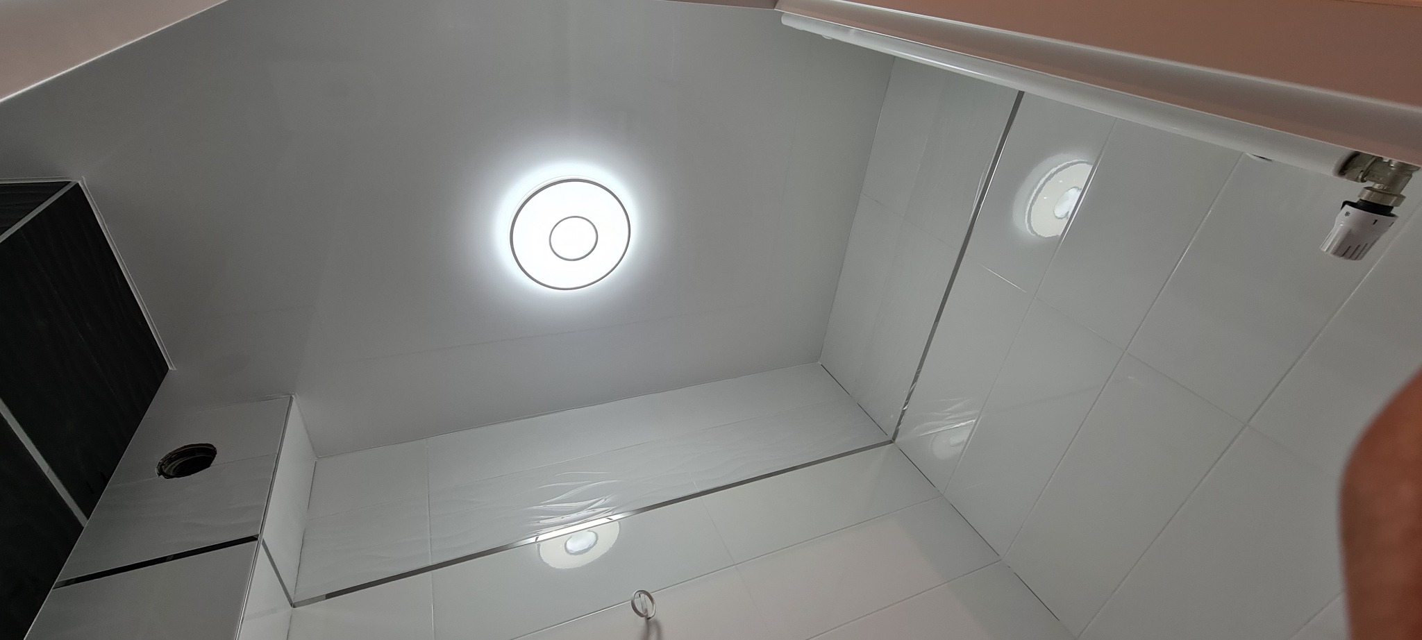 Nowoczesna kabina prysznicowa z białą glazurą, okrągłym oświetleniem sufitowym i termostatem, widok z dołu.