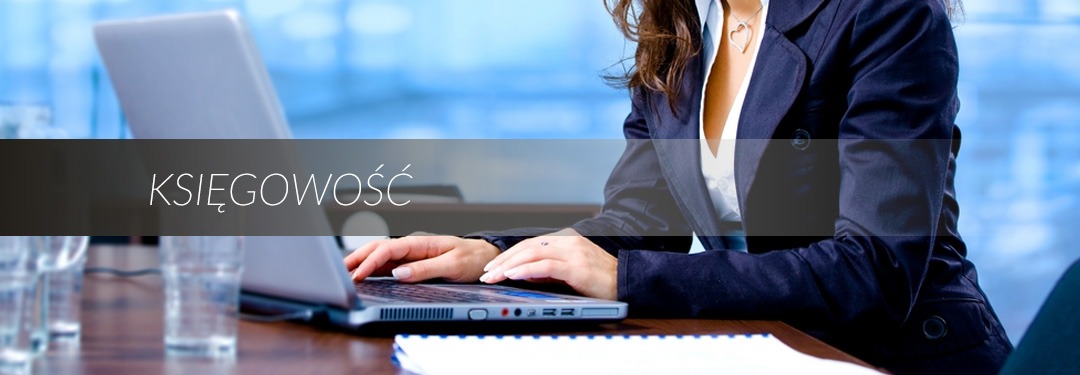 Kobieta w marynarce pracuje na laptopie przy biurku z notatnikiem, widoczne szklanki z wodą, w tle rozmyte biuro.