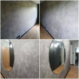 Sławomir Jurga - Ściana z efektem dekoracyjnym w odcieniach szarości, widoczne okrągłe lustro z odbiciem wnętrza mieszkania, drewniana podłoga z czarną listwą przypodłogową.