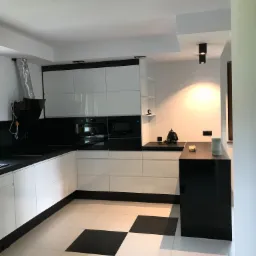 Nowoczesna, minimalistyczna kuchnia w bieli i czerni z błyszczącymi frontami, czarno-biała podłoga w szachownicę, okap z widoczną rurą wentylacyjną i punktowe oświetlenie sufitowe.