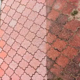 Częściowo wyczyszczona, czerwona kostka brukowa w kształcie koniczyny, widoczna różnica między czystą a brudną powierzchnią, fragment buta w prawym dolnym rogu.