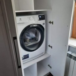 DamianMeble - Biała suszarka do ubrań Electrolux umieszczona wewnątrz białej szafy z otwartymi drzwiami, widoczny fragment grzejnika.