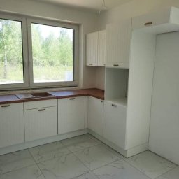 DamianMeble - Jasna kuchnia z białymi, frezowanymi frontami szafek i drewnianym blatem, widok na zielony las za oknem.