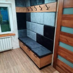 DamianMeble - Wnęka z siedziskiem i wieszakami, obita panelami tapicerowanymi w odcieniach szarości i czerni, drewniana podłoga i drzwi z przeszkleniami.