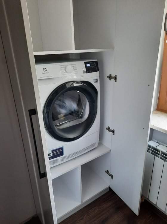 Biała suszarka do ubrań Electrolux umieszczona wewnątrz białej szafy z otwartymi drzwiami, widoczny fragment grzejnika.
