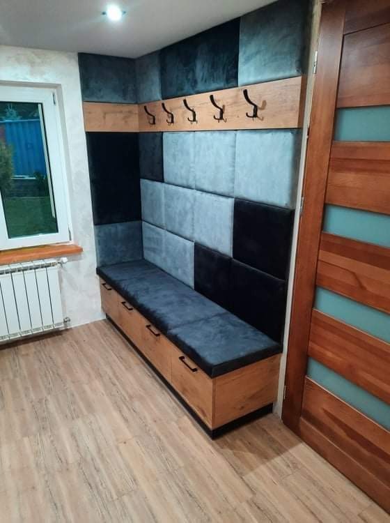 Wnęka z siedziskiem i wieszakami, obita panelami tapicerowanymi w odcieniach szarości i czerni, drewniana podłoga i drzwi z przeszkleniami.