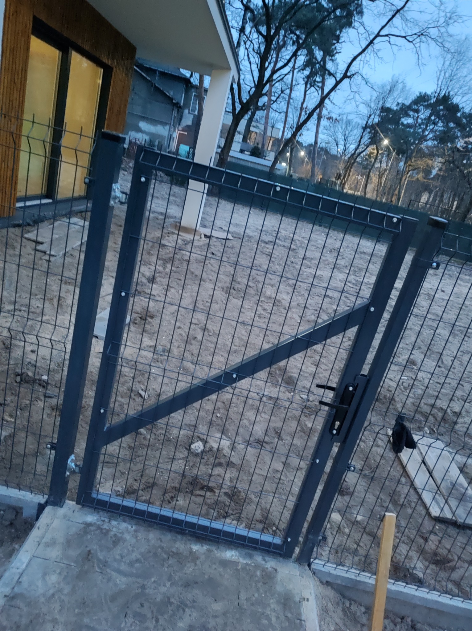 Nowo zamontowana, ocynkowana furtka z paneli ogrodzeniowych w kolorze grafitowym, widoczna z bliska na tle przygotowanego terenu pod trawnik.