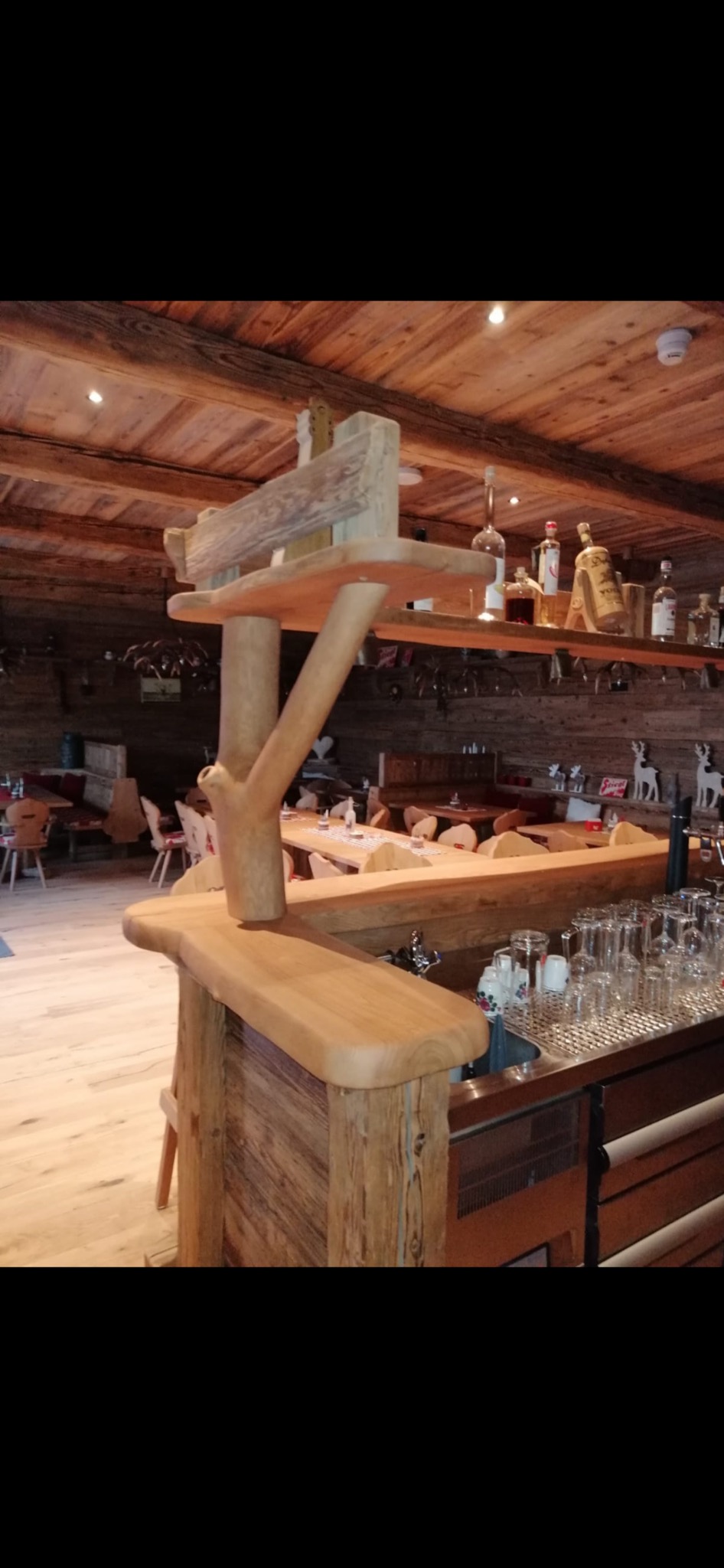 Bar z elementami z surowego drewna w rustykalnym wnętrzu restauracji, widoczne szklanki, butelki i drewniane dekoracje na półkach.