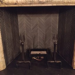 Inglot.glazura kompleksowe usługi glazurnicze - Wykończony kominek z czarną, ułożoną w jodełkę okładziną, flankowany marmurowymi kolumnami i ozdobnymi, metalowymi pogrzebaczami w kształcie głów zwierząt.