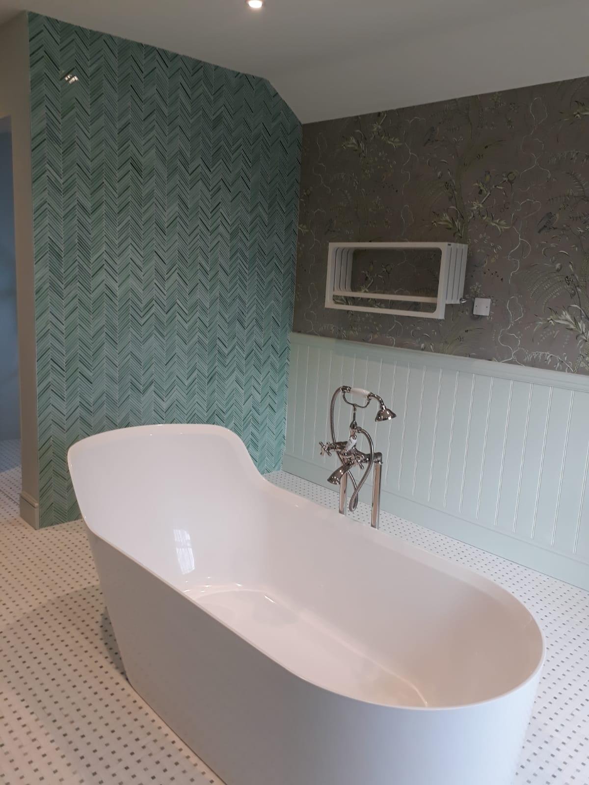 Nowoczesna łazienka z wolnostojącą białą wanną, mozaiką na podłodze i ścianie z wzorem jodełki w odcieniach zieleni, oraz panelami ściennymi w kolorze miętowym.