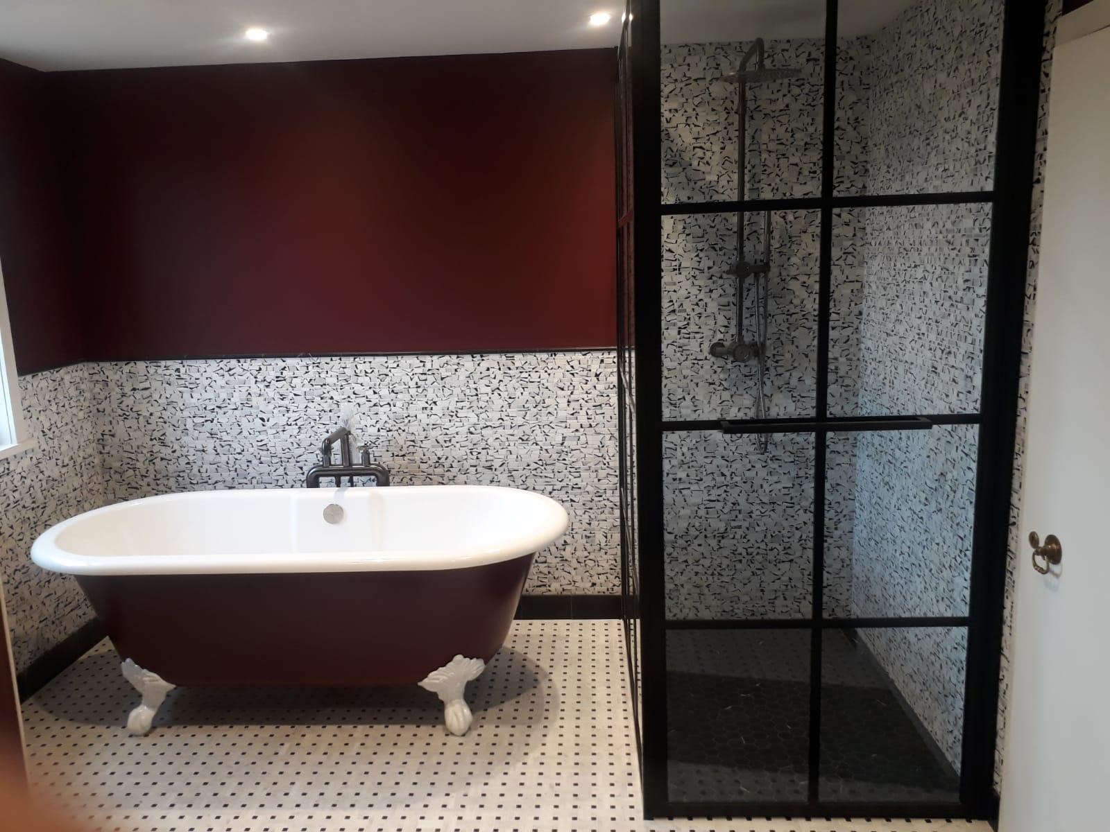 Burgundowa wanna wolnostojąca na ozdobnych nóżkach, czarno-biała mozaika na podłodze i ścianach, kabina prysznicowa z czarnymi szprosami, ściana pomalowana na burgundowo w górnej części łazienki.