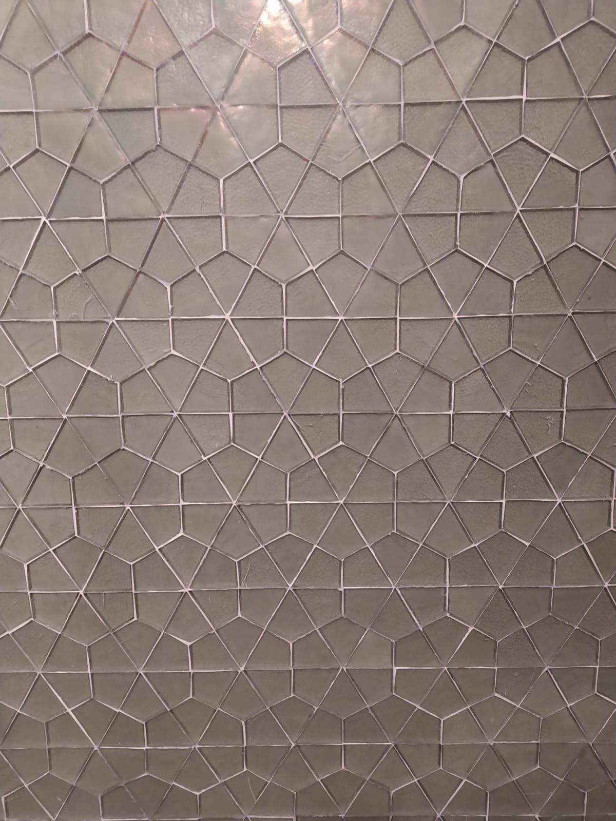 Mozaika z szarych, geometrycznych płytek o nieregularnych kształtach, połączonych białymi fugami, tworząca powtarzalny wzór gwiazdy.