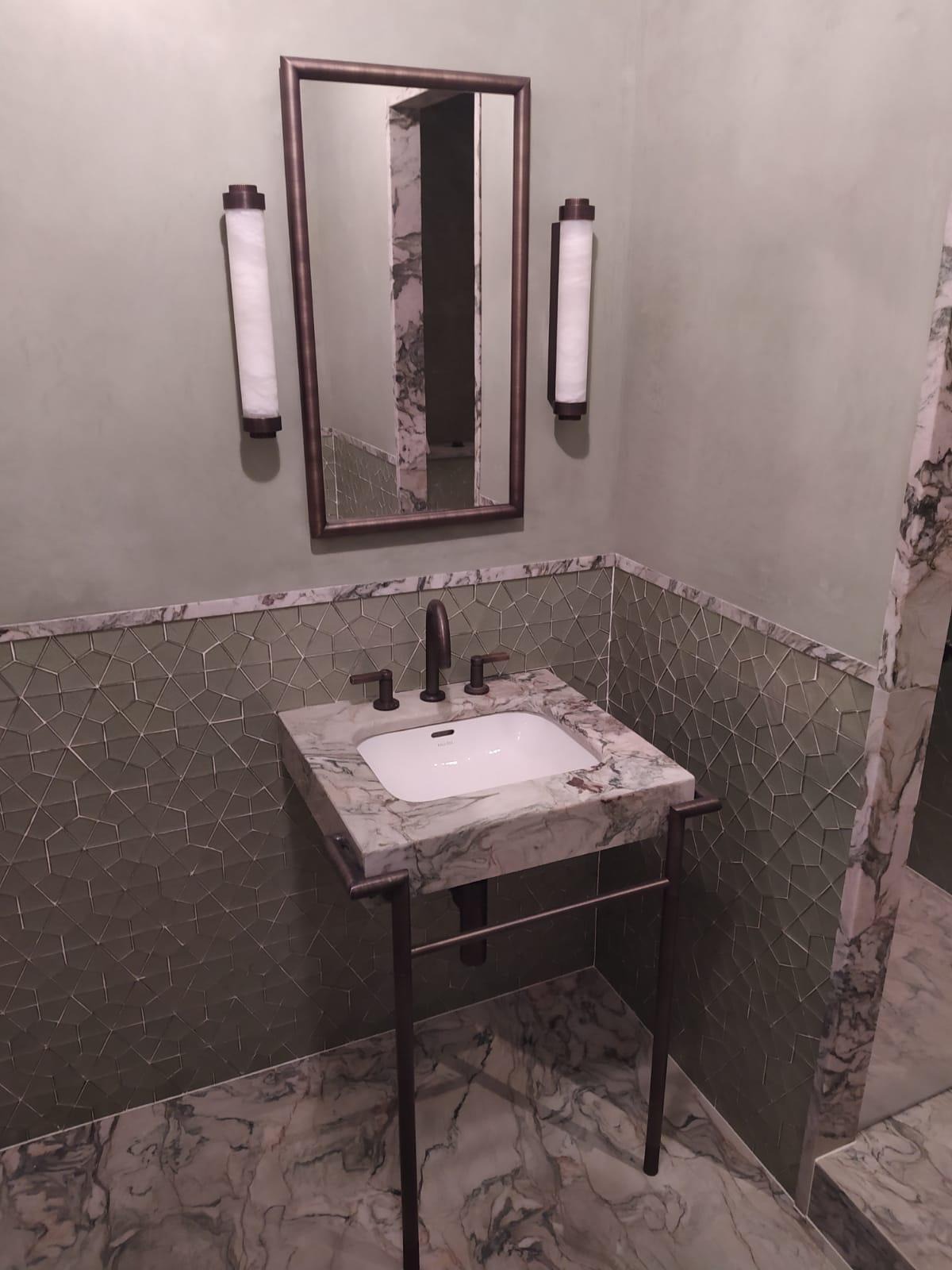 Elegancka łazienka z umywalką z marmuru Carrara na metalowym stelażu, mozaiką na ścianach w odcieniach zieleni i lustrem z oświetleniem w stylu art deco.