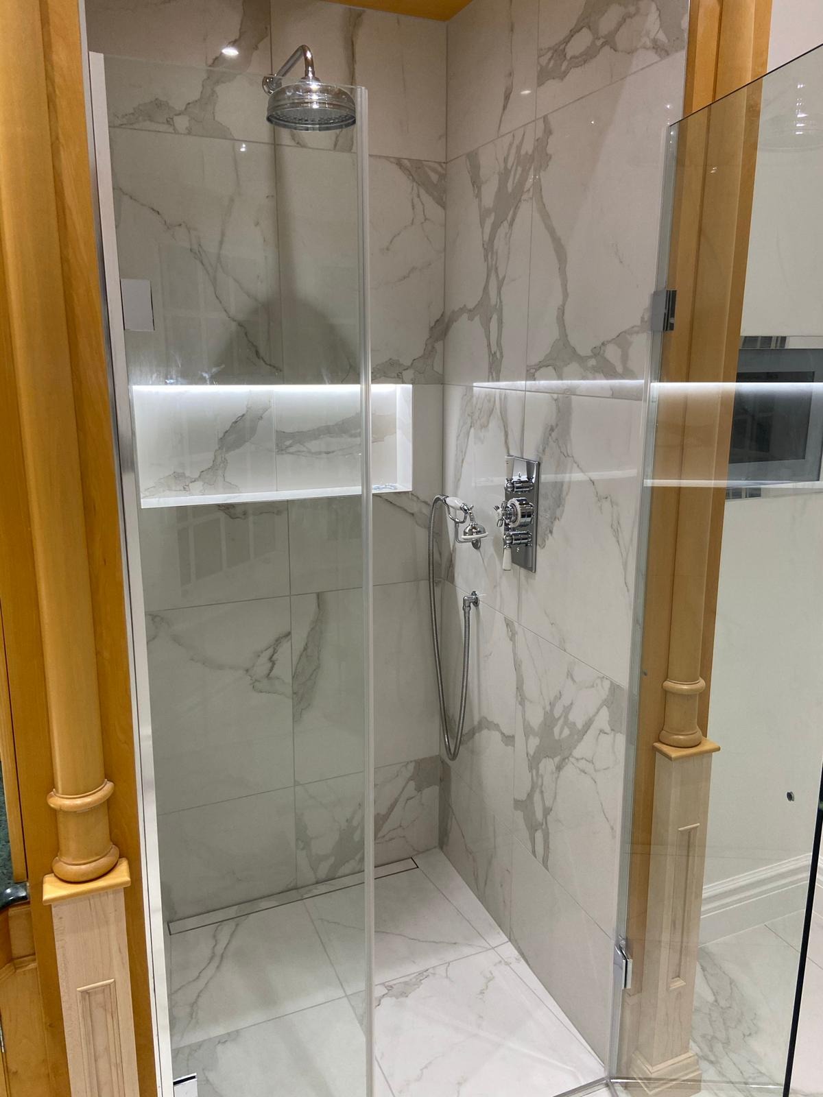 Nowoczesna kabina prysznicowa z marmurowymi płytkami, szklaną ścianką i drewnianymi elementami wykończeniowymi. Wnęka z podświetleniem LED.