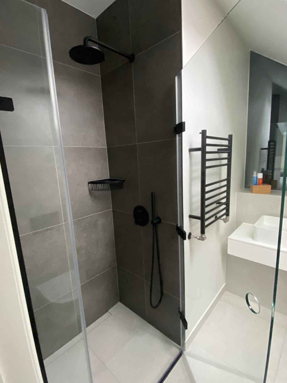 Nowoczesna kabina prysznicowa z czarną armaturą, szarymi płytkami i grzejnikiem drabinkowym w łazience po remoncie.