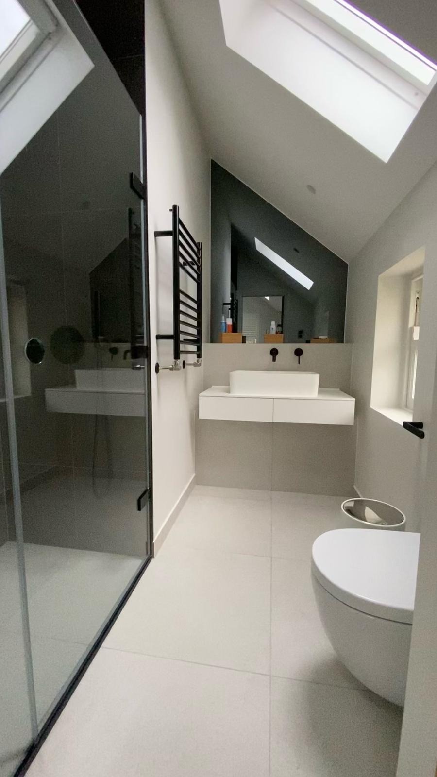 Nowoczesna łazienka na poddaszu z kabiną prysznicową ze szkła, umywalką nablatową na szafce, grzejnikiem drabinkowym i oknem dachowym.