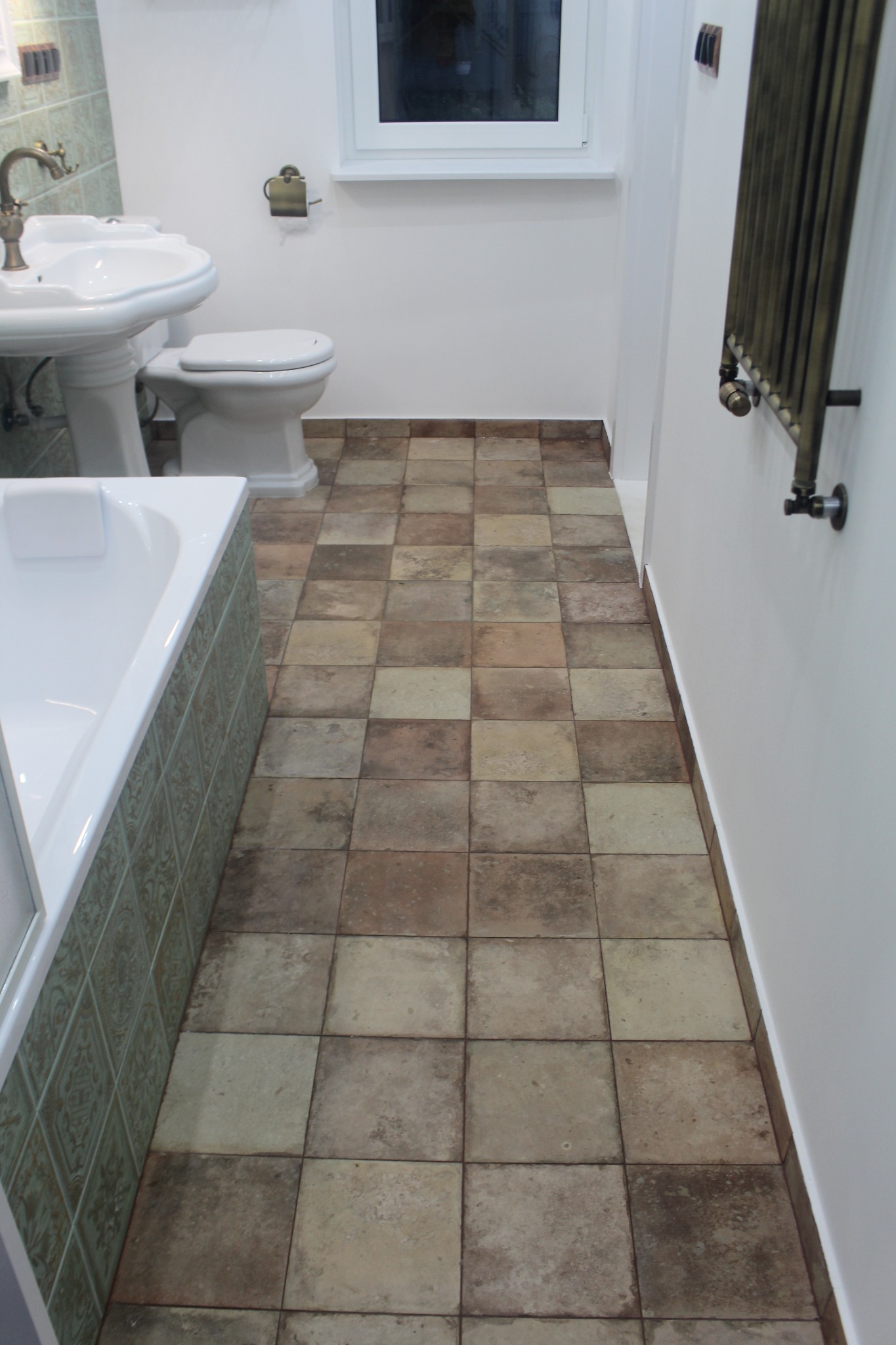 Wykończona łazienka z beżowo-brązową podłogą z płytek, białą ceramiką sanitarną i grzejnikiem w stylu retro.