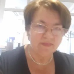 Portret kobiety w okularach i srebrnym naszyjniku, w tle okno biurowe.