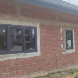 Damar Damian Głowacki - Montaż okien PCV w surowym budynku z czerwonej cegły, widoczne ślady zaprawy wokół ram okiennych.