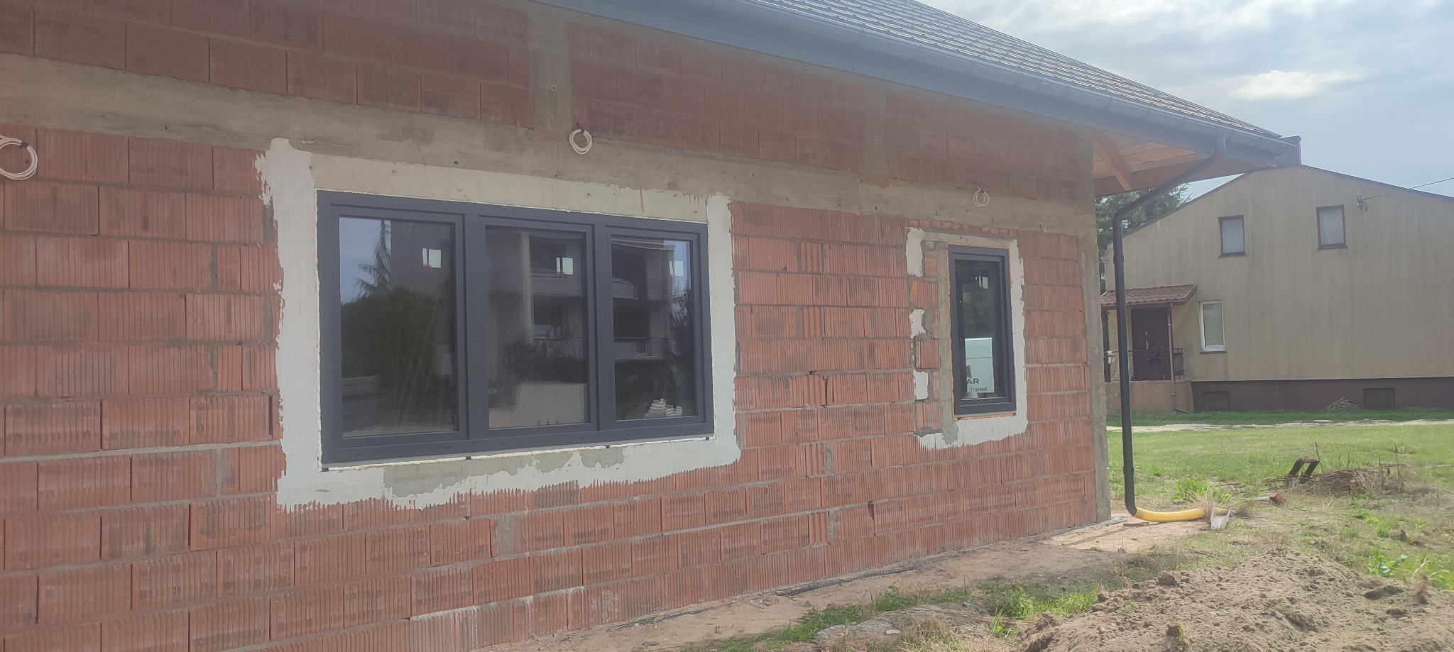 Montaż okien PCV w surowym budynku z czerwonej cegły, widoczne ślady zaprawy wokół ram okiennych.