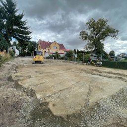 DEJV-BUD Dawid Trzebniak - Żółta minikoparka i zagęszczarka na wyrównanym terenie pod budowę domu jednorodzinnego, widok na budynek i pochmurne niebo.