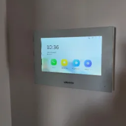 Panel dotykowy domofonu Hikvision zamontowany na ścianie, wyświetlający ekran główny z ikonami połączeń, wiadomości, podglądu na żywo i ustawień.