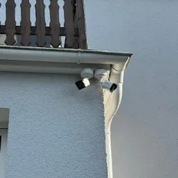 Dwie kamery monitoringu Hikvision zamontowane pod okapem budynku z balkonem z drewnianą balustradą