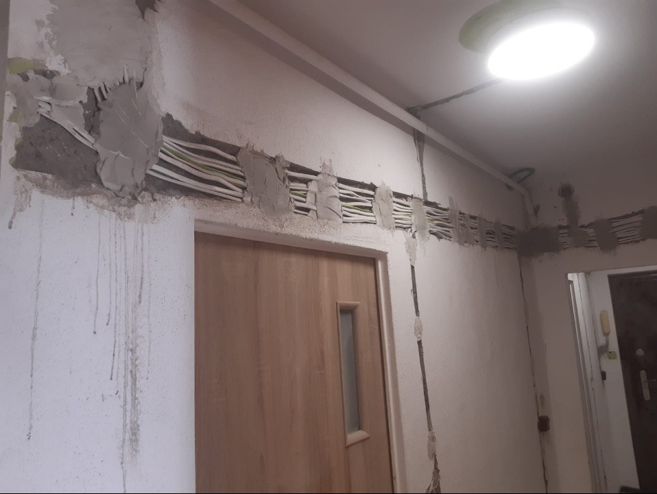 Kable elektryczne ułożone w bruzdach w ścianie, częściowo zamaskowane gipsem, widoczne w korytarzu nad drzwiami.