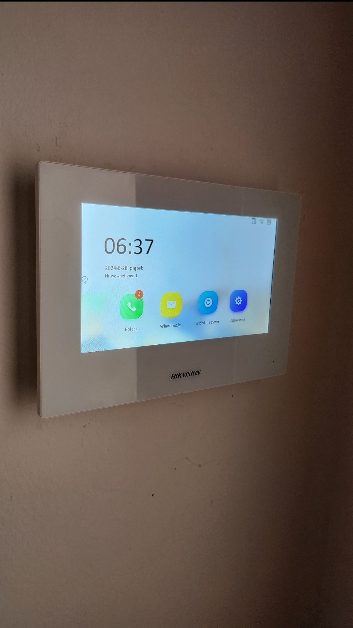 Zamontowany na ścianie panel wideodomofonu Hikvision z widocznym ekranem głównym, prezentującym godzinę 06:37, datę 28 czerwca 2024 oraz ikonę połączenia z liczbą 3 powiadomień.